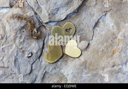 Three bright beautiful metal hearts are placed on a rock with natural salt on a beach. Stock Photo
