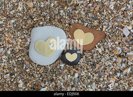 Three bright beautiful metal hearts are placed on three different rocks on sandy background. Stock Photo