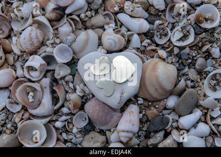 Three bright beautiful metal hearts are placed on a rock with shells in the backgound Stock Photo