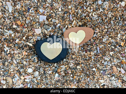 Two bright beautiful metal hearts are placed on two different rocks on sandy background. Stock Photo