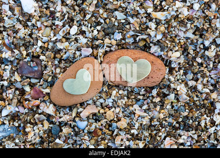 Two bright beautiful metal hearts are placed on two red rocks on sandy background. Stock Photo