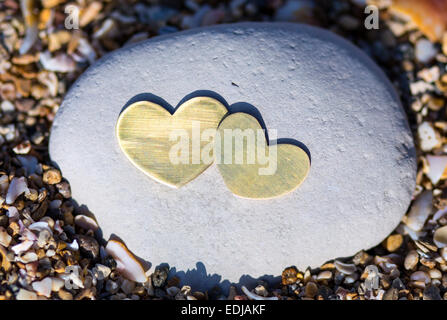 Two bright beautiful metal hearts are placed on a bright rock on sandy background. Stock Photo
