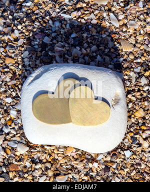 Two bright beautiful metal hearts are placed on a bright rock on sandy background. Portrait orientation. Stock Photo