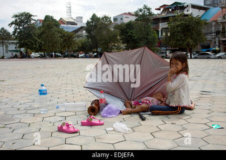 A young girl attends to her sibling who is shaded by an umbrella in Freedom Park in Phnom Penh, Cambodia. Stock Photo