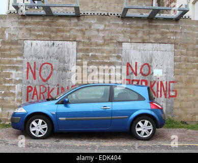 Car parked in front of 'no parking' painted sign on brick wall and boards Stock Photo