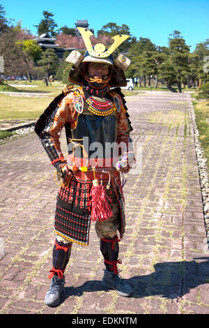 Japanese man standing in full samurai armour suit and helmet, suji bachi Kabuto, made entirely from compressed paper. Matsu castle in background. Stock Photo