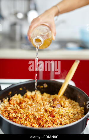Woman adding white wine to lasagna recipe in a pan on the stove