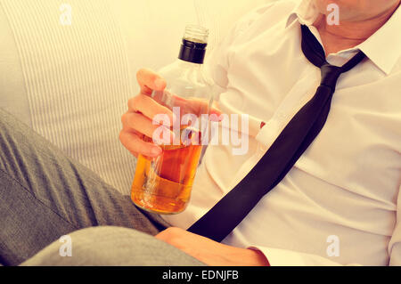 a young with his necktie loosened is drinking alcohol from a bottle Stock Photo