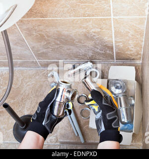 Sanitary technician repairs plumbing trap from sink in bathroom Stock Photo
