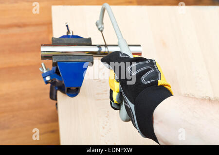 plumber sawing plumbing drain pipe gripped in vice on wooden table by hacksaw Stock Photo