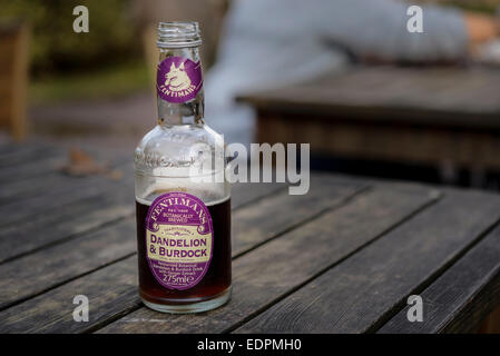 A half-finished bottle of Fentiman's dandelion and burdock soft drink soda on a wooden picnic table. Stock Photo