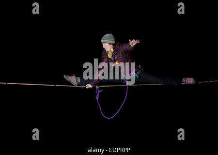 Professional highliner Hayley Ashburn in winter clothing doing the splits on a highline in the dark Stock Photo