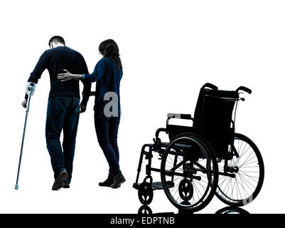 one man injured man with woman walking away from wheelchair with crutches in silhouette studio on white background Stock Photo