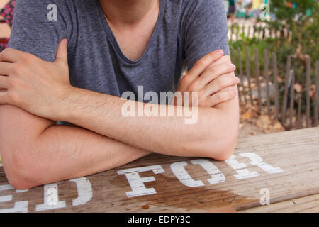 Close-up of a young man's crossed arms at a beer garden table. Stock Photo