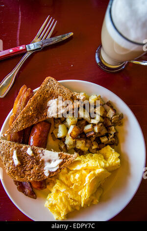 A plate of breakfast food including toast, bacon, potatoes and eggs with a latte on the side at a restaurant in California. Stock Photo