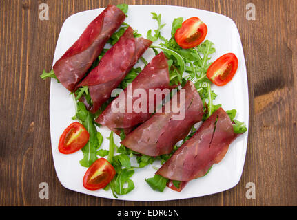 Rolls of dried beef on plate over wooden table seen from above Stock Photo