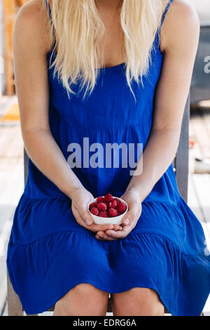 Young woman in blue dress holding a white bowl containing raspberries