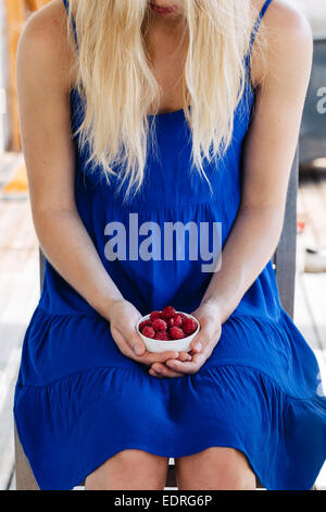 Young woman in blue dress holding a white bowl containing raspberries