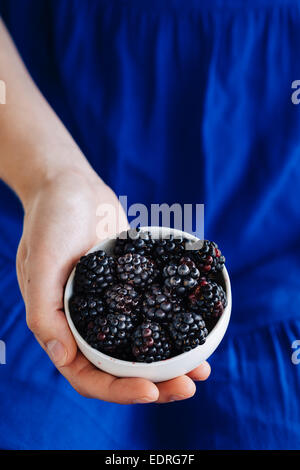 Young woman in blue dress holding a white bowl containing blackberries Stock Photo