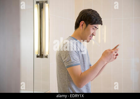 Young man texting in bathroom Stock Photo