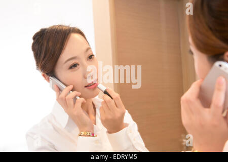 Young woman on mobile putting on lipstick Stock Photo