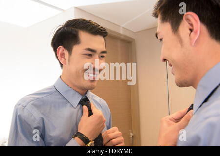 Young man putting on tie in front of mirror Stock Photo