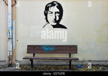 Famous musician John Lennon from The Beatles portrait stencil graffiti on textured wall and wooden bench. Stock Photo
