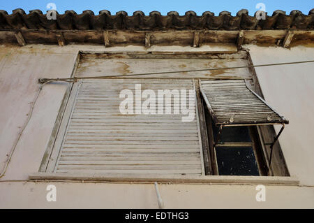 Rusty window shutter and stained white wall. Abandoned house exterior. Stock Photo