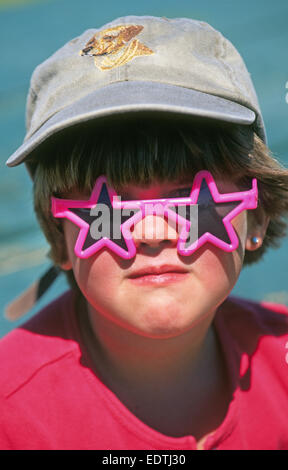 A ten year old girl wearing a baseball cap and plastic sunglasses looking like a tomboy. Stock Photo