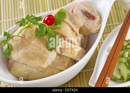 Chinese sliced roasted chicken in white bowl with sliced cucumber as side dish under natural bamboo place mat Stock Photo