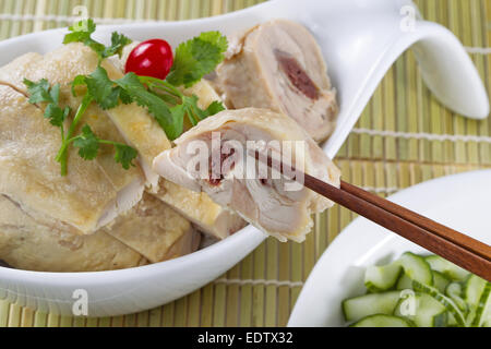 Chinese sliced roasted chicken, with chopsticks holding a single piece, in white bowl with sliced cucumber Stock Photo