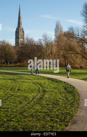 View of Salisbury Cathedral spire from Queen Elizabeth Gardens in Mill Road. People walking along the path towards spire. Stock Photo