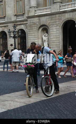 Tourist couple on bikes, lost and looking at map in Plaça de Sant Jaume, Barcelona. Stock Photo