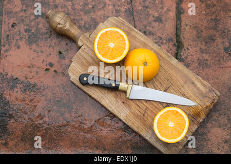 sliced oranges on an old wooden board with cutting knife, against terracotta tile wet surface background Stock Photo