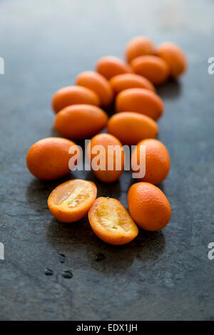 scattering of vibrant orange backlit kumquats, on green marble background Stock Photo