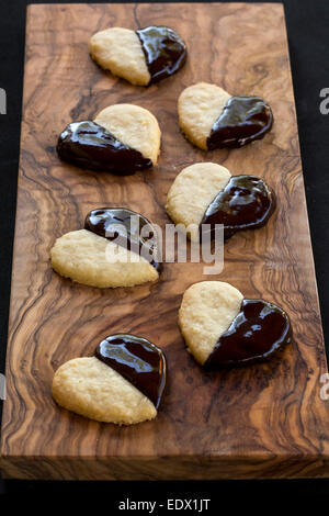 homemade chocolate dipped heart biscuits or cookies on olive wood board Stock Photo