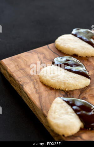 homemade chocolate dipped heart biscuits or cookies on olive wood board, against black background Stock Photo