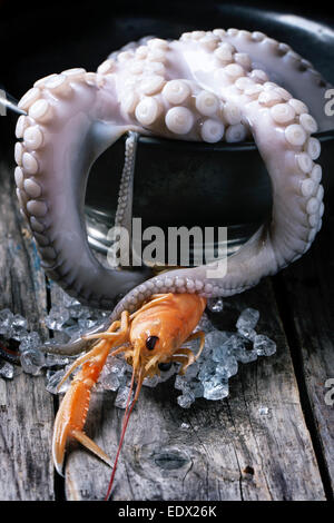 Raw langoustine and octopus tentacles with ice on old wooden table Stock Photo