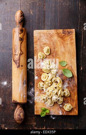 Homemade raw Tortellini and basil leaves on dark wooden background Stock Photo