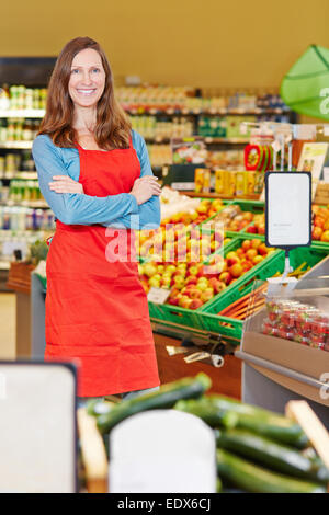 Smiling elderly saleswoman standing in a supermarket with her arms crossed Stock Photo