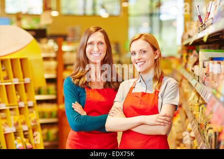 Two friendly saleswomen smiling in a supermarket with her arms crossed Stock Photo