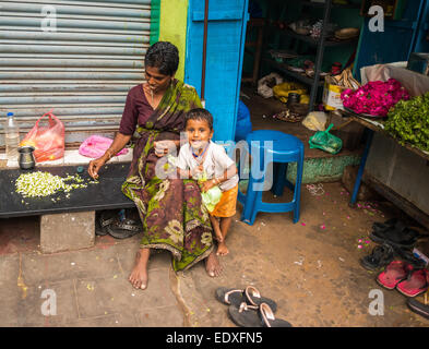 THANJAVOUR, INDIA - FEBRUARY 14: An unidentified child and a woman in traditional Indian attire are sitting. Woman weaves a garl Stock Photo