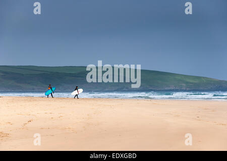 Surfers making their way to the sea, carrying their boards on Crantock beach near Newquay, Cornwall. Stock Photo
