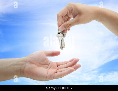 hand giving set of house keys against blue sky and sun Stock Photo