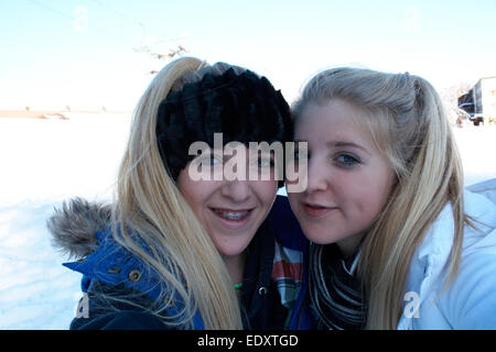 two teenage blonde haired girls taking a selfie on a skiing holiday in switzerland Stock Photo