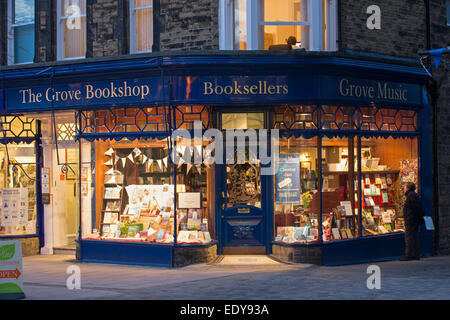 Man outside looks at window display books in The Grove Bookshop (traditional book shop, welcoming golden glow of lights) - Ilkley, West Yorkshire, UK. Stock Photo