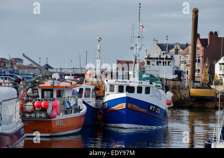 Small, colourful fishing boats or vessels, are moored side by side in the water of sunny, scenic Whitby harbour - North Yorkshire coast, England, UK. Stock Photo