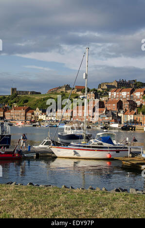 Sunny summertime view of yachts & boats moored in the Marina with St Mary's Church & Abbey on cliff beyond - Whitby harbour, Yorkshire, England, UK. Stock Photo