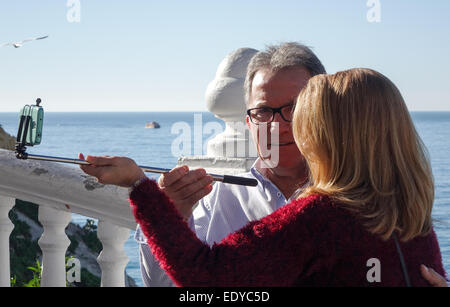Mature couple taking selfy using selfie stick and cell phone, mobile phone picture on sunny day at the sea side in Benidorm. Stock Photo