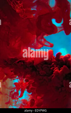 Vivid abstract macro photograph of crimson red and cyan ink dispersing through water, creating dramatic swirling cloud-like formations. Stock Photo